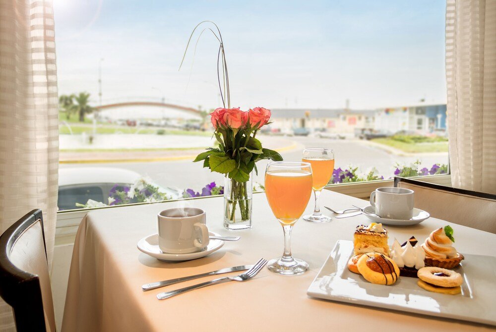Mesa de desayuno con café, jugo de naranja, copa de vino y facturas